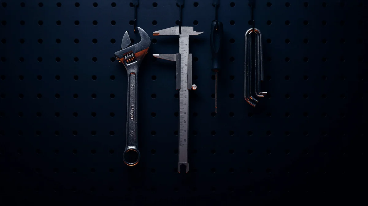 A dark pegboard wall with precision hand tools hanging in silhouette, a wrench, a caliper, a screwdriver, representing the tools an agent uses to take real action in company systems