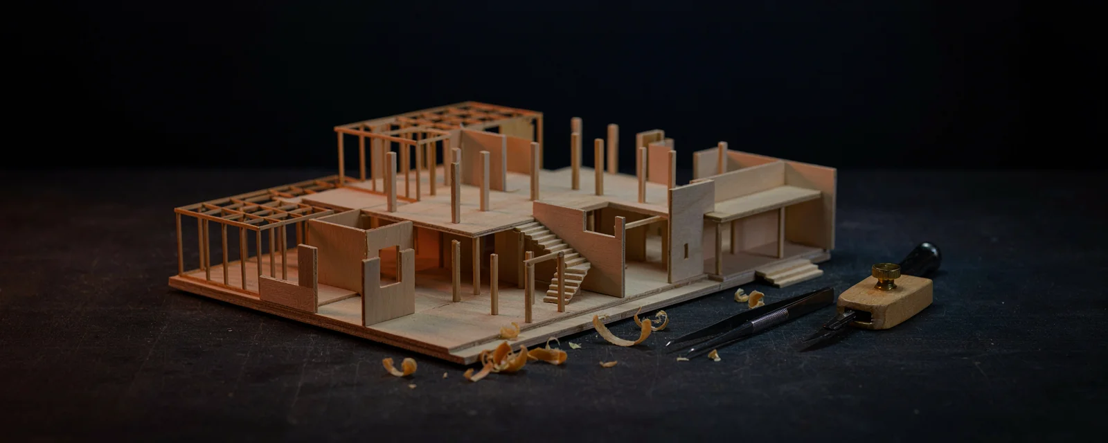 A small precise architectural scale model under construction from wooden blocks, representing building the smallest working version first
